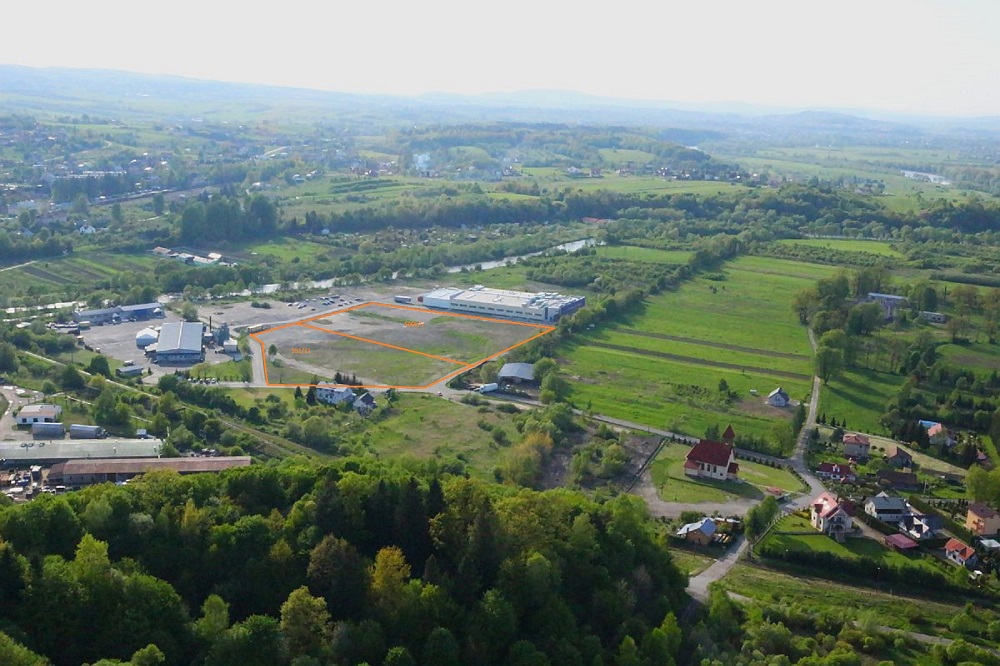 Zdjęcie lotnicze krajobrazu z budynkami, polami i lasami, z zaznaczonym terenem inwestycyjnym.